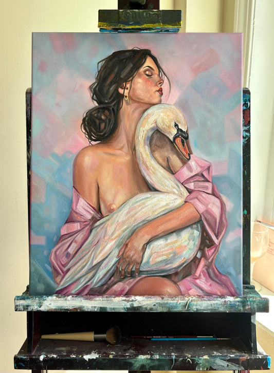 An oil painting on canvas depicting a woman embracing a white swan, displayed on a paint-covered artist's easel in an indoor studio setting.