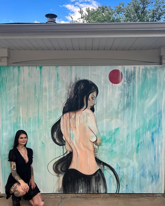 Gracey Ripa standing in front of a large vertical artwork on canvas, which depicts a stylized, partial nude figure with long hair against a predominantly blue background with abstract elements.