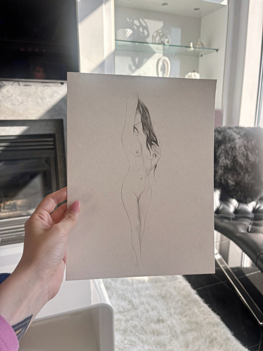 Hand holding a piece of paper with a sketched nude figure in a room.