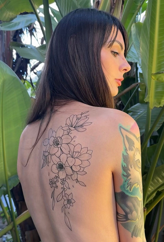 Gracey Ripa posing with a beautiful, decorative, floral temporary tattoo on her back. She is standing in a sunny garden with banana leaves around her. 