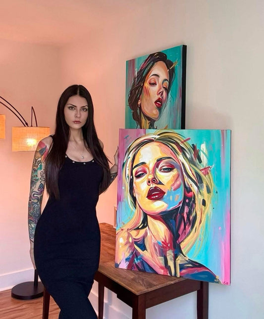 Gracey Ripa standing next to two colorful artworks of women's faces on a wall.