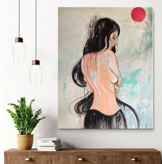 A vertical canvas art print depicting a woman from behind with long black hair, a red sun, and a soft pastel background, displayed on a white wall above a wooden console table with a potted plant and books.