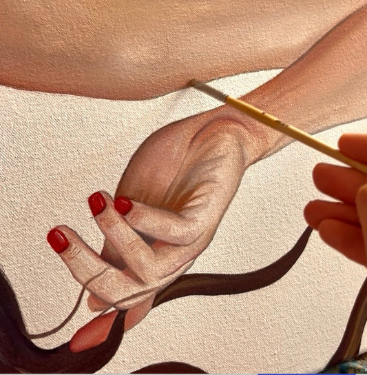 Close-up of a hand with red nail polish holding a paintbrush, with another hand gently touching it on a beige background.