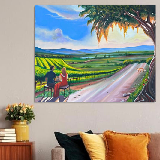 A colorful landscape canvas print depicting a couple sitting by a vineyard road, hung on a beige wall above a sofa with decorative pillows.