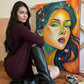 Gracey Ripa sitting in front of a painting of a woman's face. 
