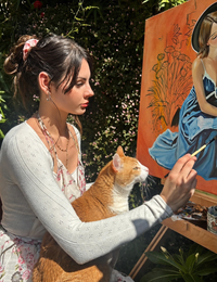 Gracey painting outdoors with an orange cat on her lap